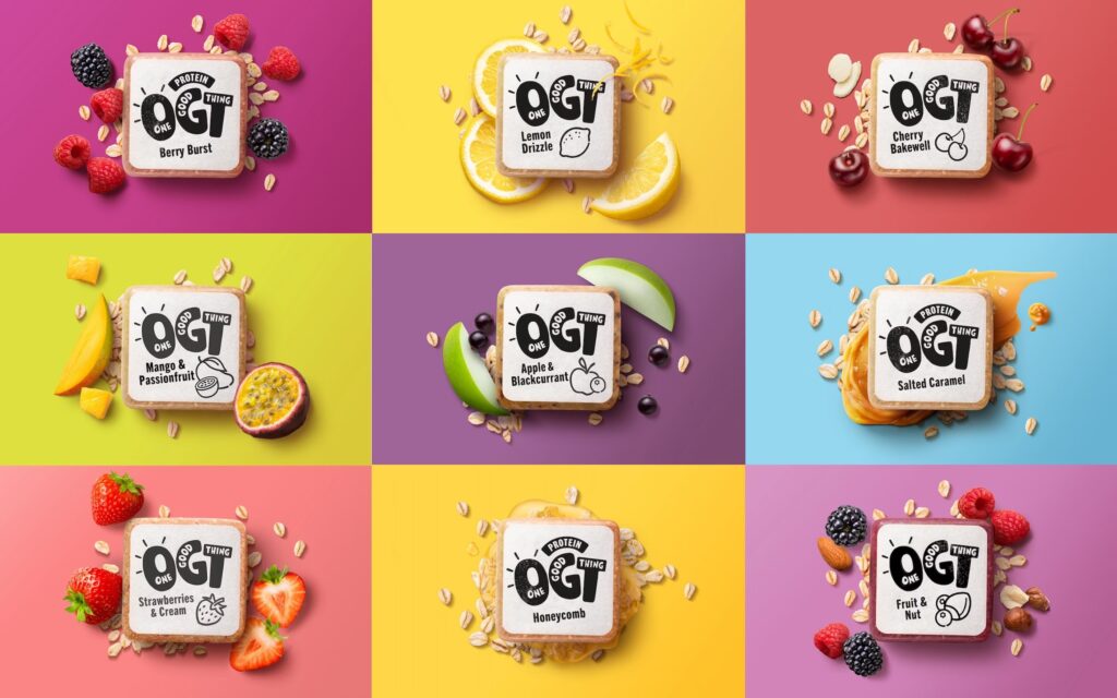 Grid of OGT protein snack bars in nine flavors including Berry Burst, Lemon Drizzle, Cherry Bakewell, Mango & Passionfruit, Apple & Blackcurrant, Salted Caramel, Strawberries & Cream, Honeycomb, and Fruit & Nut, displayed with fresh ingredients on colorful backgrounds