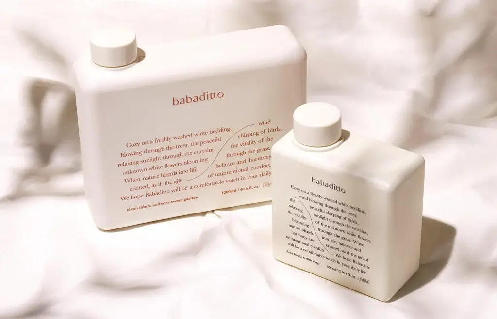 Babaditto minimalist packaging for fabric softener and dish soap in cream-colored bottles on white fabric.