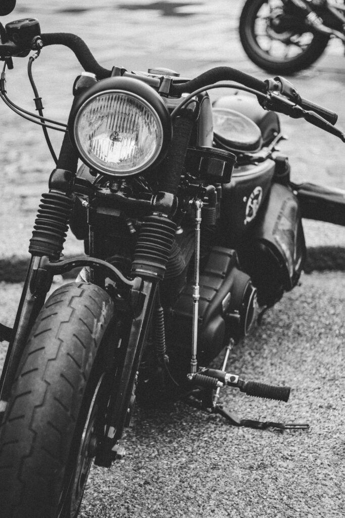 Close-up of a custom black motorcycle parked on a paved surface in black and white.