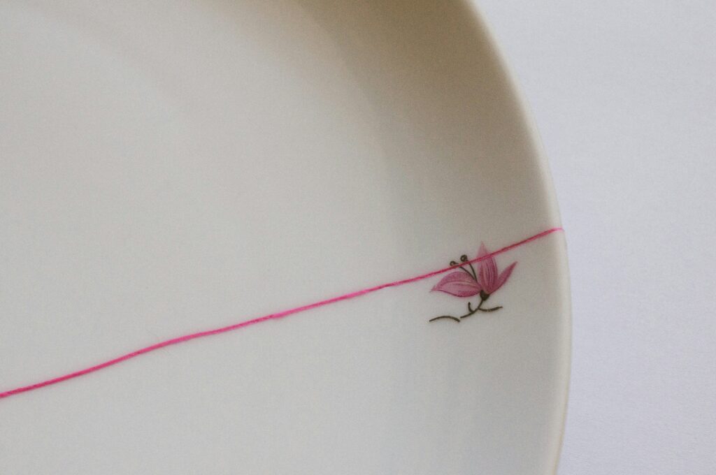 White ceramic plate repaired with a bright pink line, symbolising Kintsugi and the Wabi Sabi philosophy of imperfect beauty.