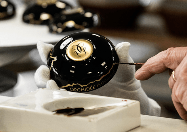 Close-up of hands applying gold detailing to a black luxury Guerlain jar, inspired by Kintsugi and Wabi Sabi
