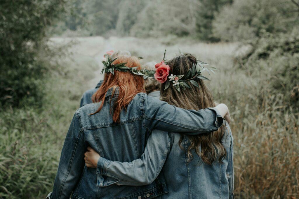 Two friends walking arm in arm outdoors wearing flower crowns, representing the Galentine’s Day cultural movement and friendship