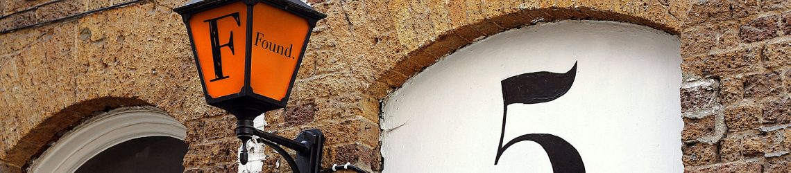 Lamp post with 'F' and 'Found' written on it next to a large number 5 on a brick wal